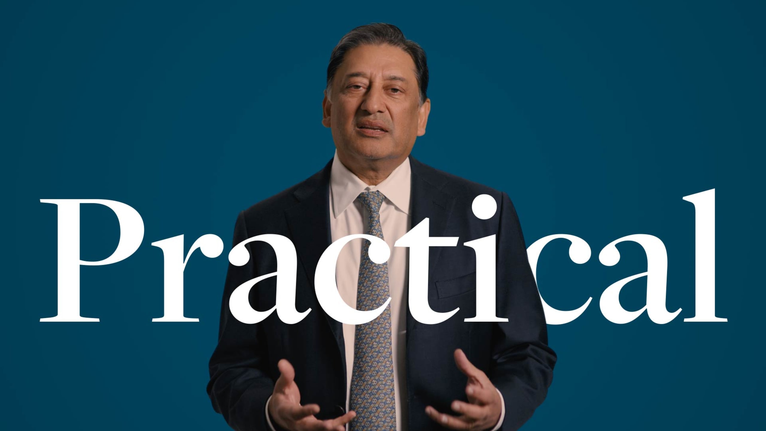 Man in a suit gestures while speaking, with the word "Practical" in large text over a blue background.
