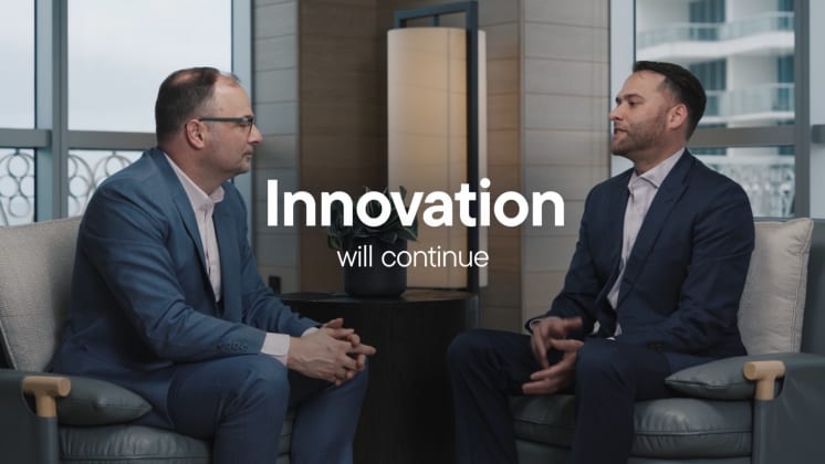 Two men in suits sit facing each other in an office setting. Text overlay reads "Innovation will continue."